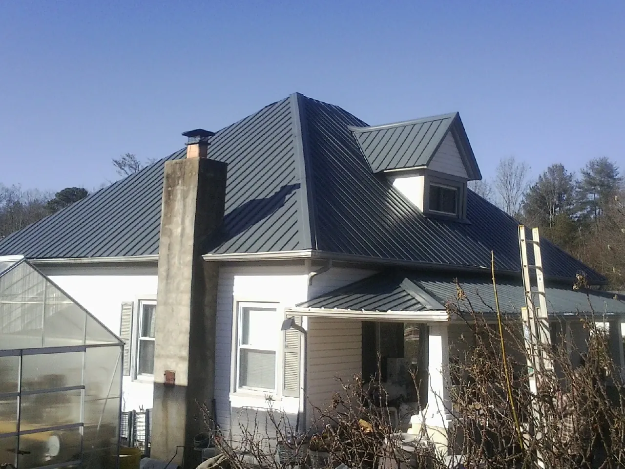 Dark blue standing seam metal roof on a white farmhouse with dormer — Slate & Tile Roof Repair by Roofing Brothers in Lower Salem