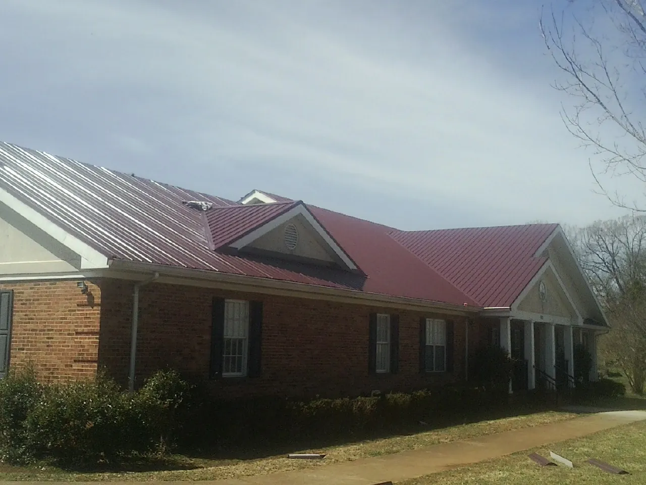 Red metal roof with gabled entries on a long brick building, from a Hail Damage Roof Repair job in Lower Salem