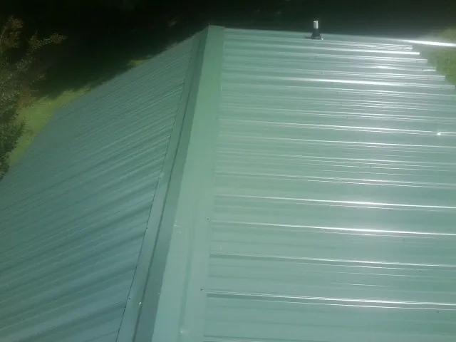 New green metal panels meeting at the ridge of a roof — Flat Roof Repair work by our crew in Lower Salem