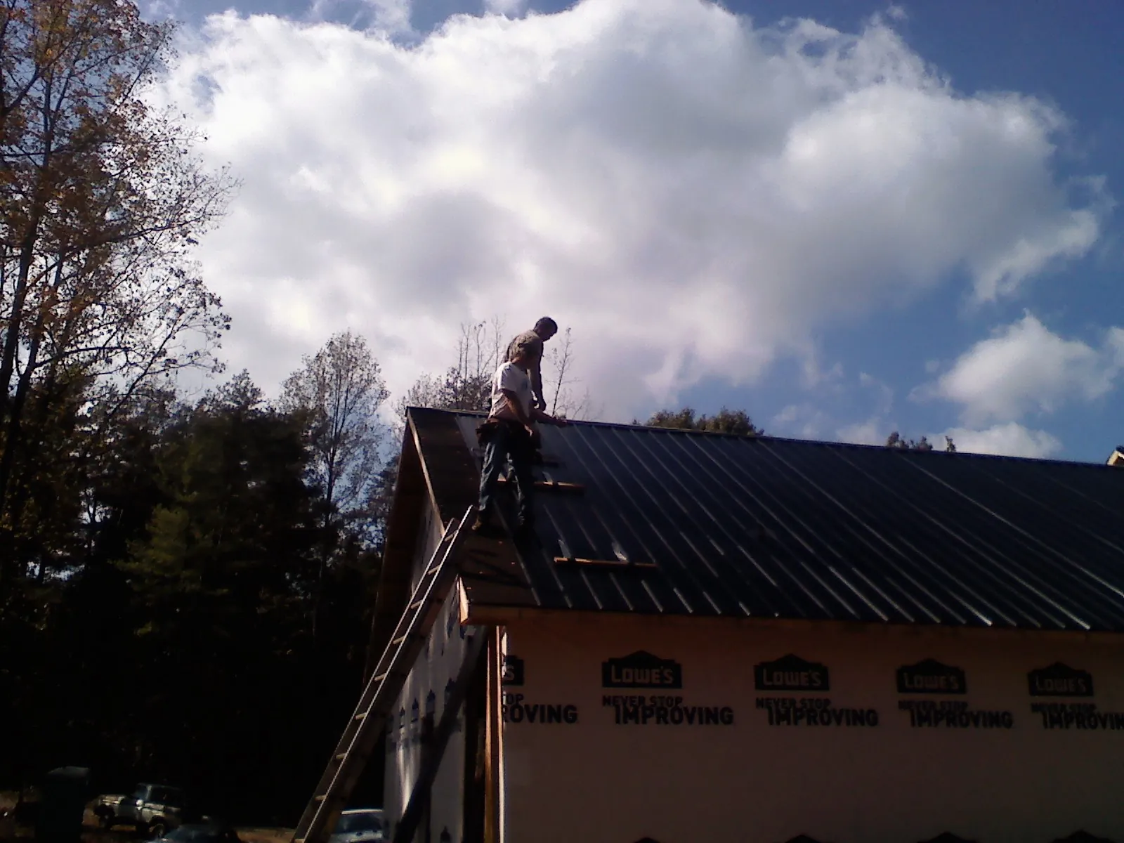 Roofer fastening dark metal panels high against a cloudy sky, from a Roof Inspection job in Lower Salem