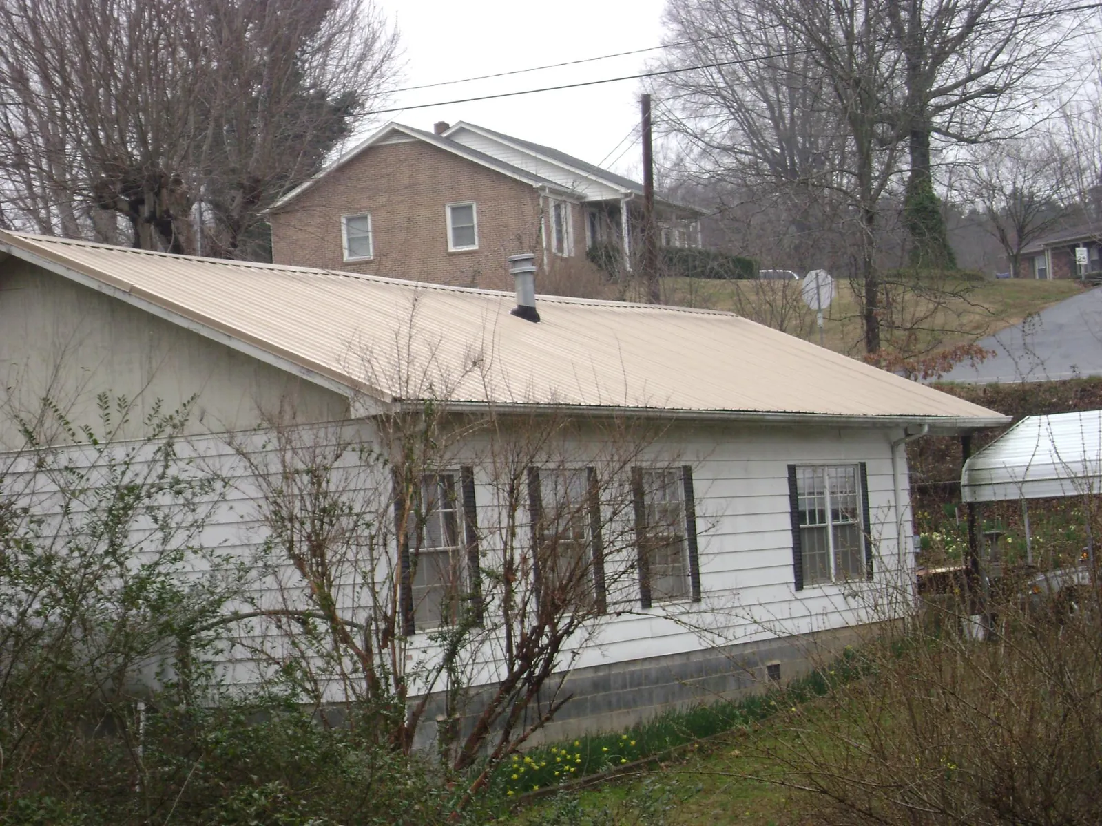 Tan metal roof on a white sided house set into a hillside — Commercial Roofing by Roofing Brothers in Lower Salem
